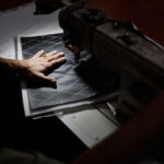 Close up of male worker sewing car upholstery detail with industrial sewing machine at factory, accent light