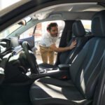 Focused auto dealership customer looking inside motor vehicle while touching front passenger seat